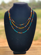 Load image into Gallery viewer, A western style 3 strand necklace. black, yellow, and turquoise serape patterns. 16 inches is the shortest strand, middle strand 18 inches and longest strand is 22 inches. This is cowgirl jewlery
